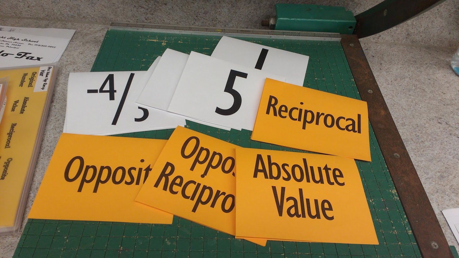 papers with numbers written on them and colored papers with text "reciprocal," "absolute value," "opposite," and "opposite reciprocal." 